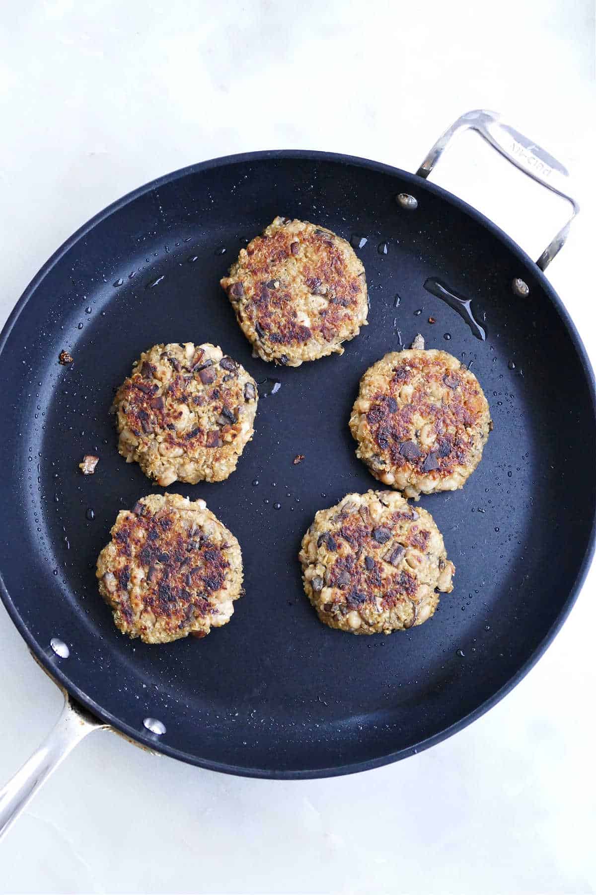 five quinoa mushroom burgers cooking in oil in a nonstick skillet