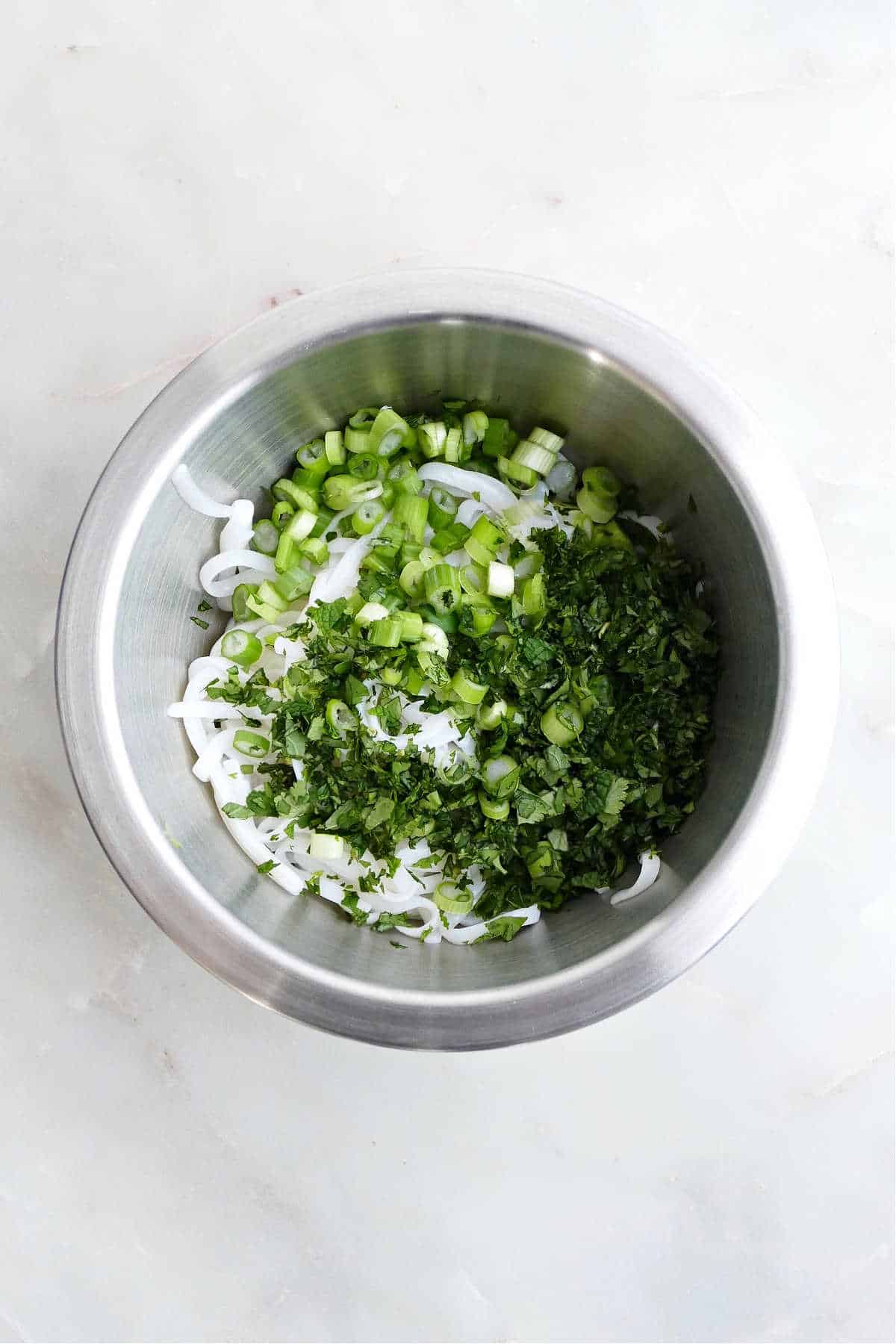 cooked rice noodles in a mixing bowl with chopped scallions and herbs