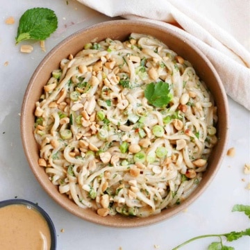 vegan peanut noodles topped with chopped peanuts and herbs in a serving bowl