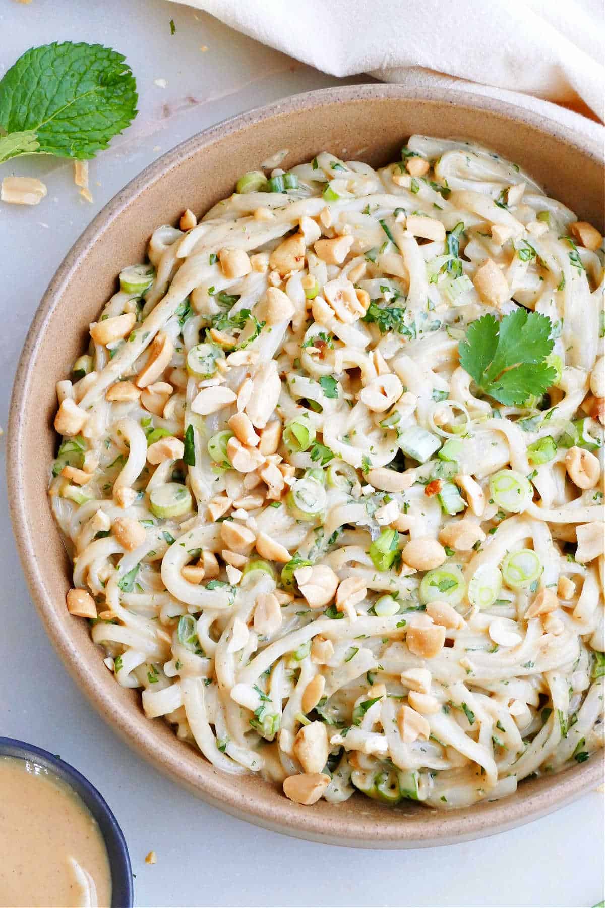 vegan peanut rice noodles with herbs, green onions, and peanuts in a mixing bowl
