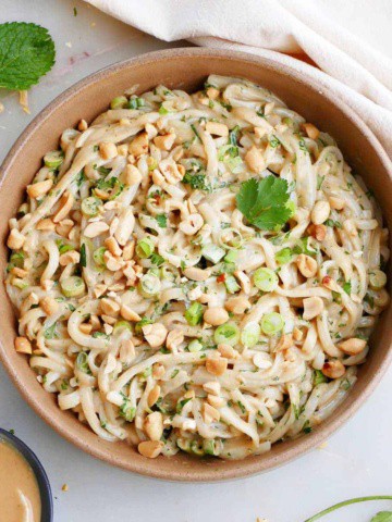 vegan peanut noodles topped with chopped peanuts and herbs in a serving bowl