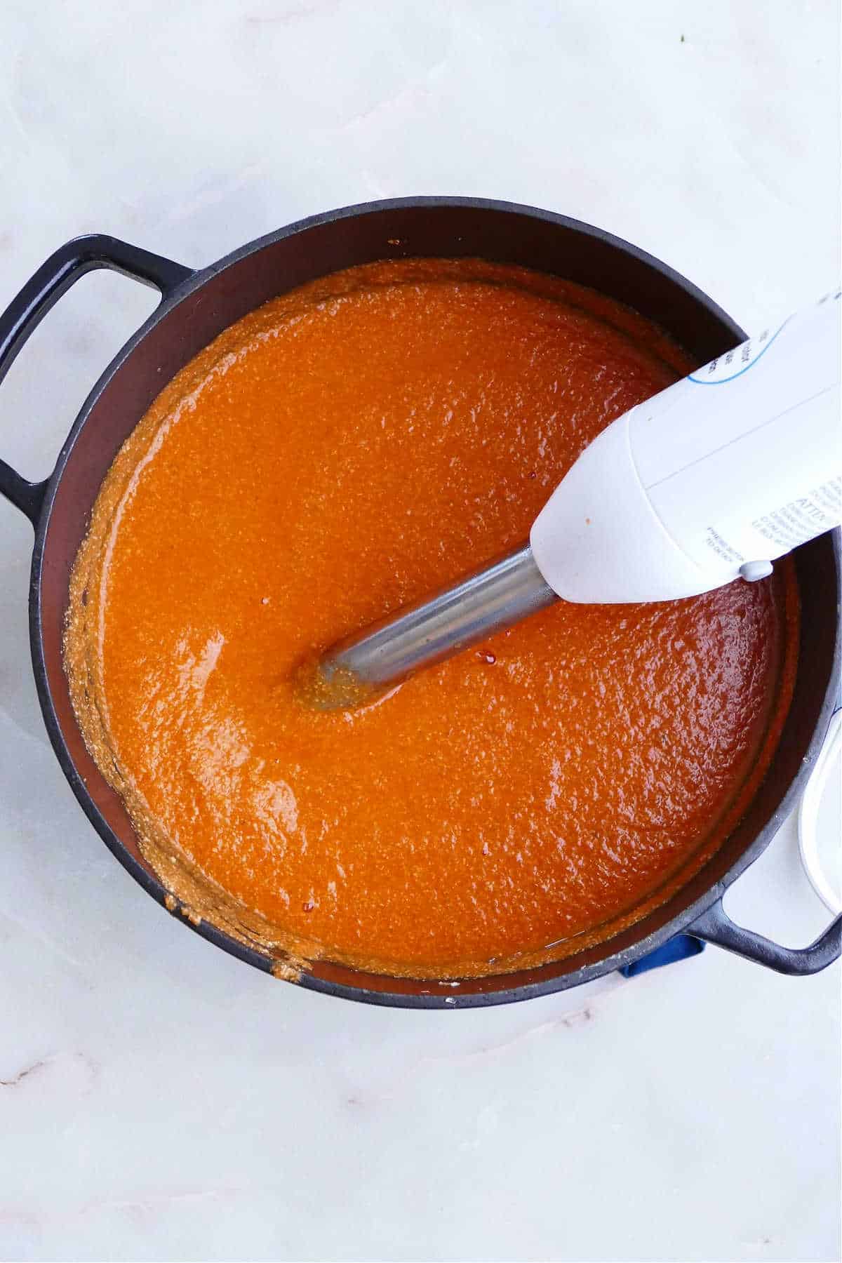 vegan tomato bisque being blended with an immersion blender in a large soup pot
