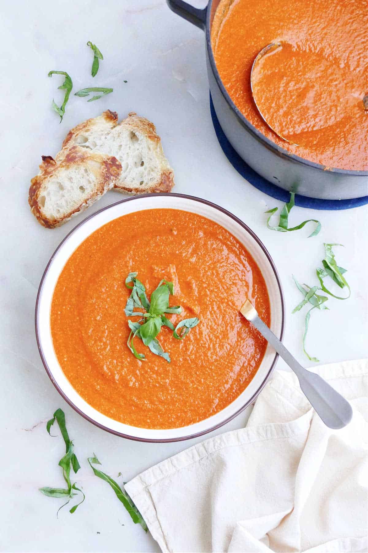 vegan tomato bisque topped with basil chiffonade in a serving bowl with a spoon