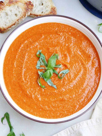 vegan tomato bisque topped with fresh basil in a bowl on a counter