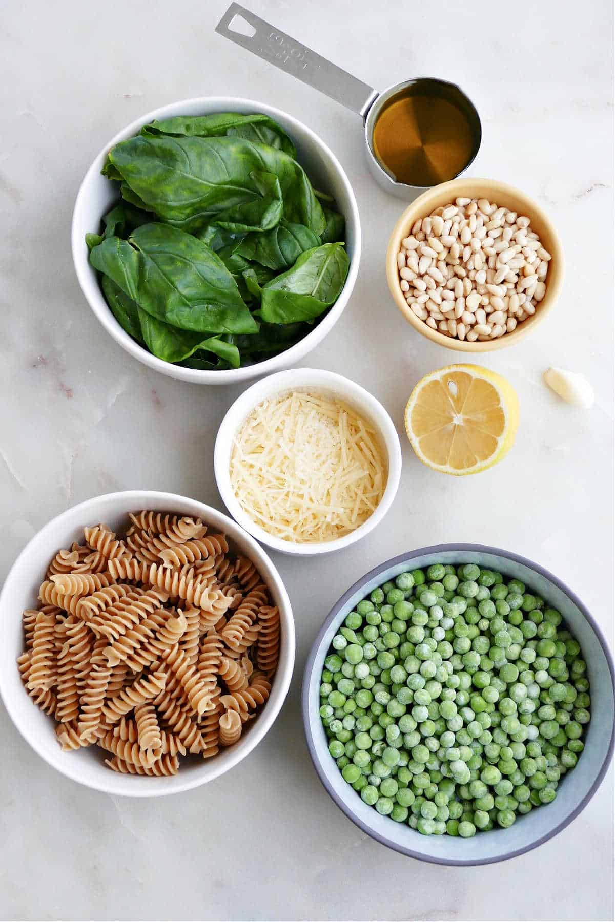 basil, olive oil, pine nuts, parmesan cheese, lemon, garlic, pasta, and peas on a counter