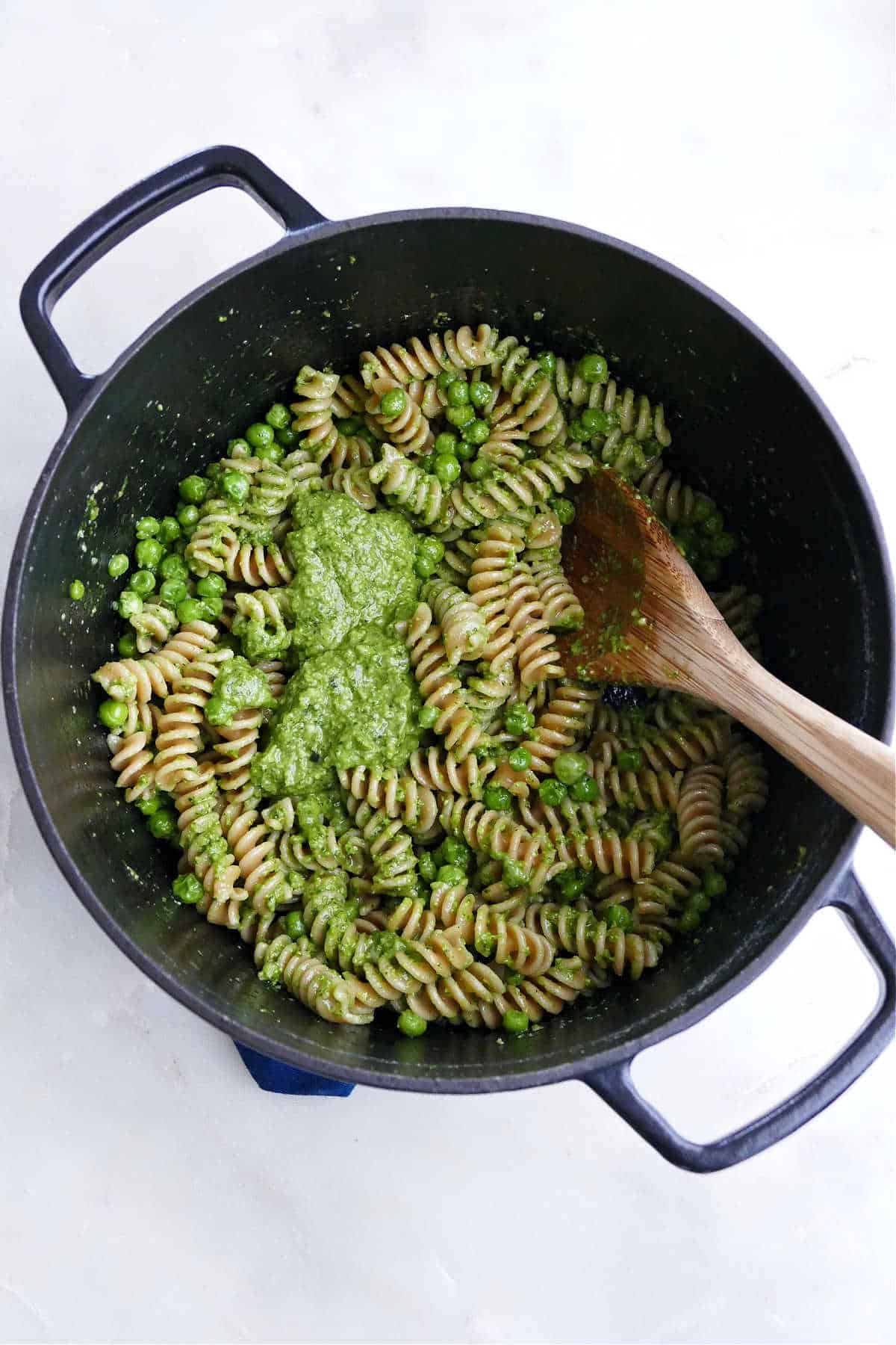fusilli pasta in a Dutch oven with peas and basil pesto being mixed in
