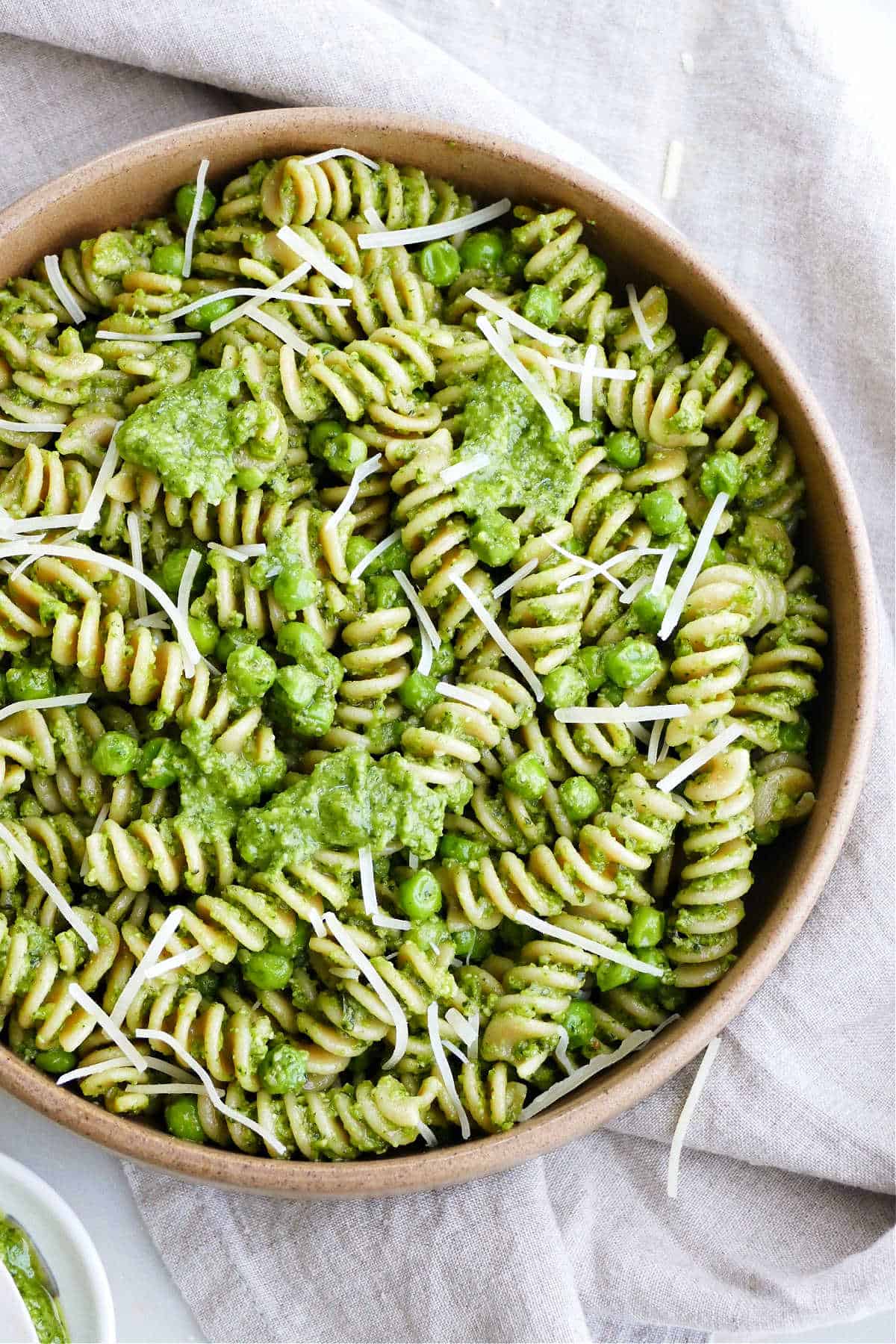 fusilli pasta with pesto, peas, and parmesan in a bowl on top of a napkin