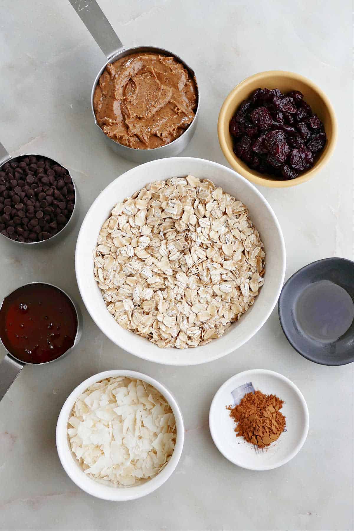 almond butter, oats, dried cherries, vanilla, cinnamon, coconut, chocolate chips, and honey on a counter