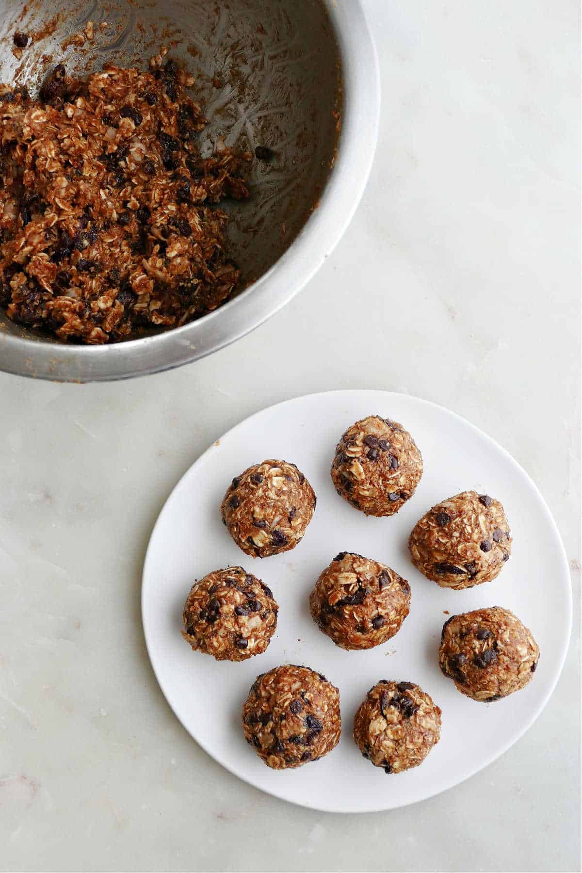 eight almond butter energy balls on a small plate next to mixing bowl with batter