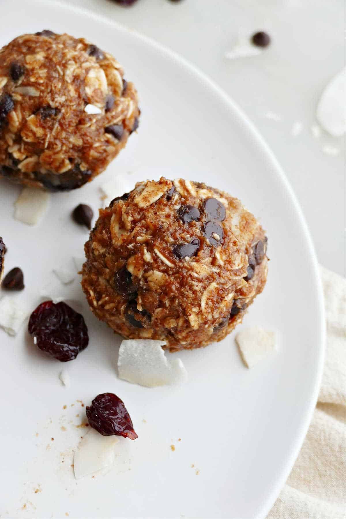 two almond butter protein bites on a serving plate sprinkled with cherries and coconut