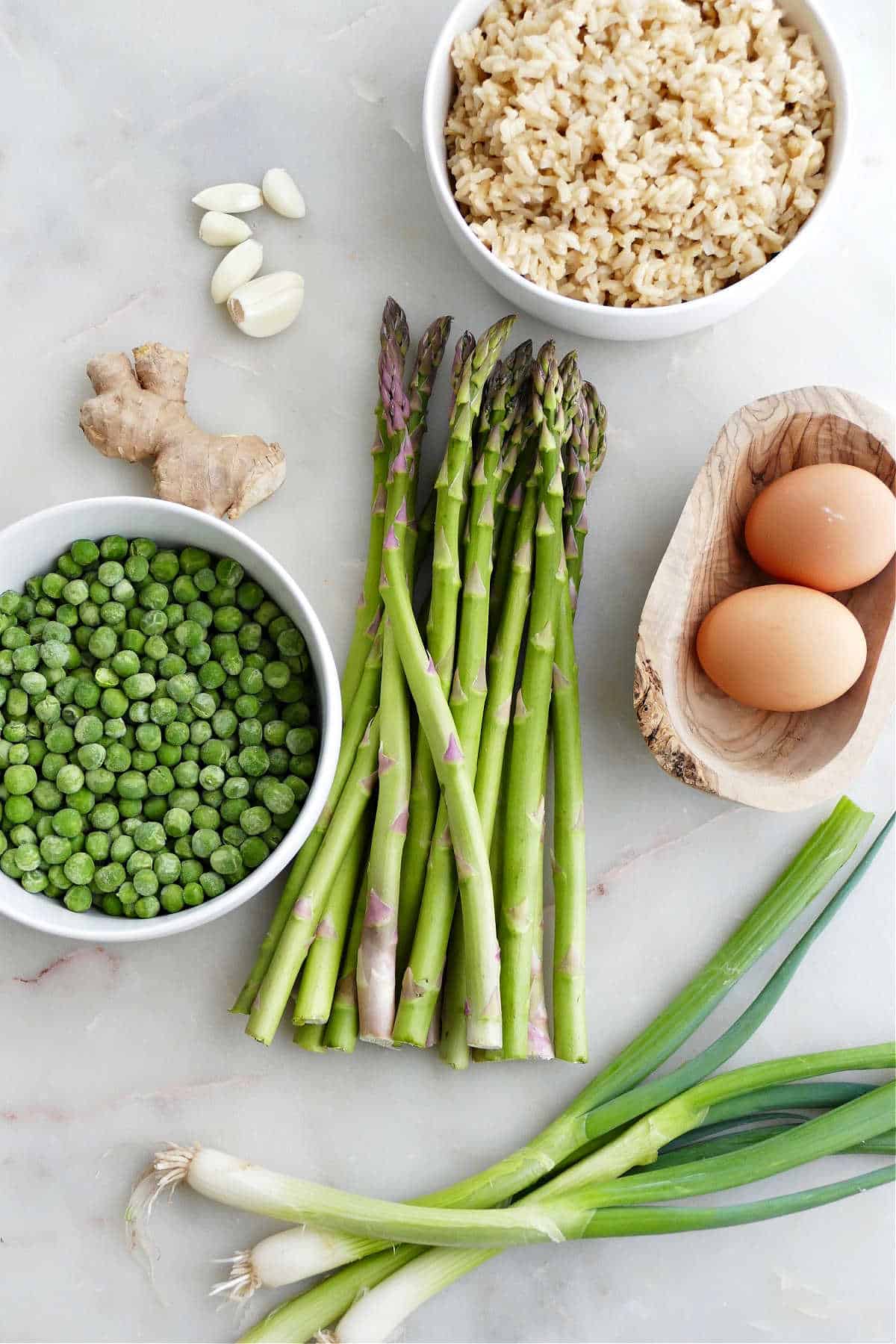 brown rice, asparagus, eggs, scallions, peas, ginger, and garlic on a counter
