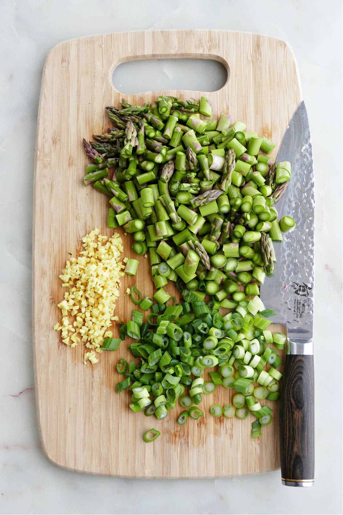 sliced asparagus and minced ginger on a cutting board next to a chef's knife