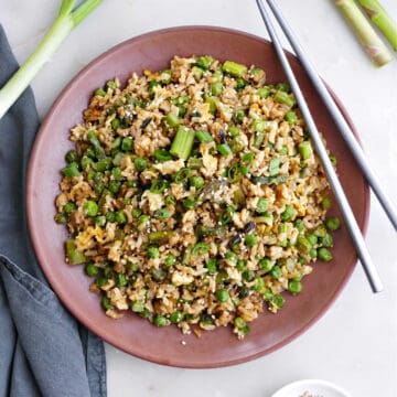 asparagus fried rice on a serving plate with chopsticks next to toppings