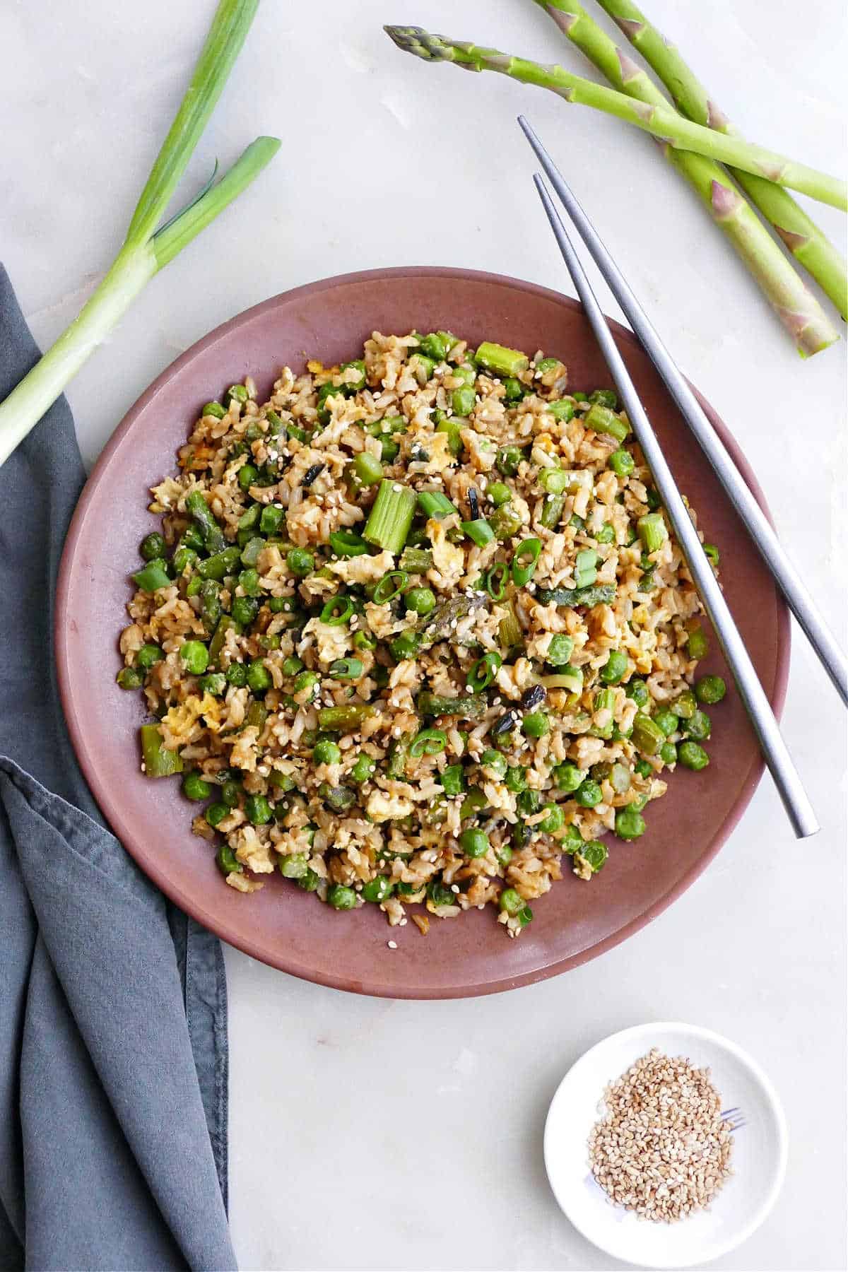 asparagus fried rice on a serving plate with chopsticks next to toppings