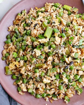asparagus fried rice on a serving plate with chopsticks next to toppings
