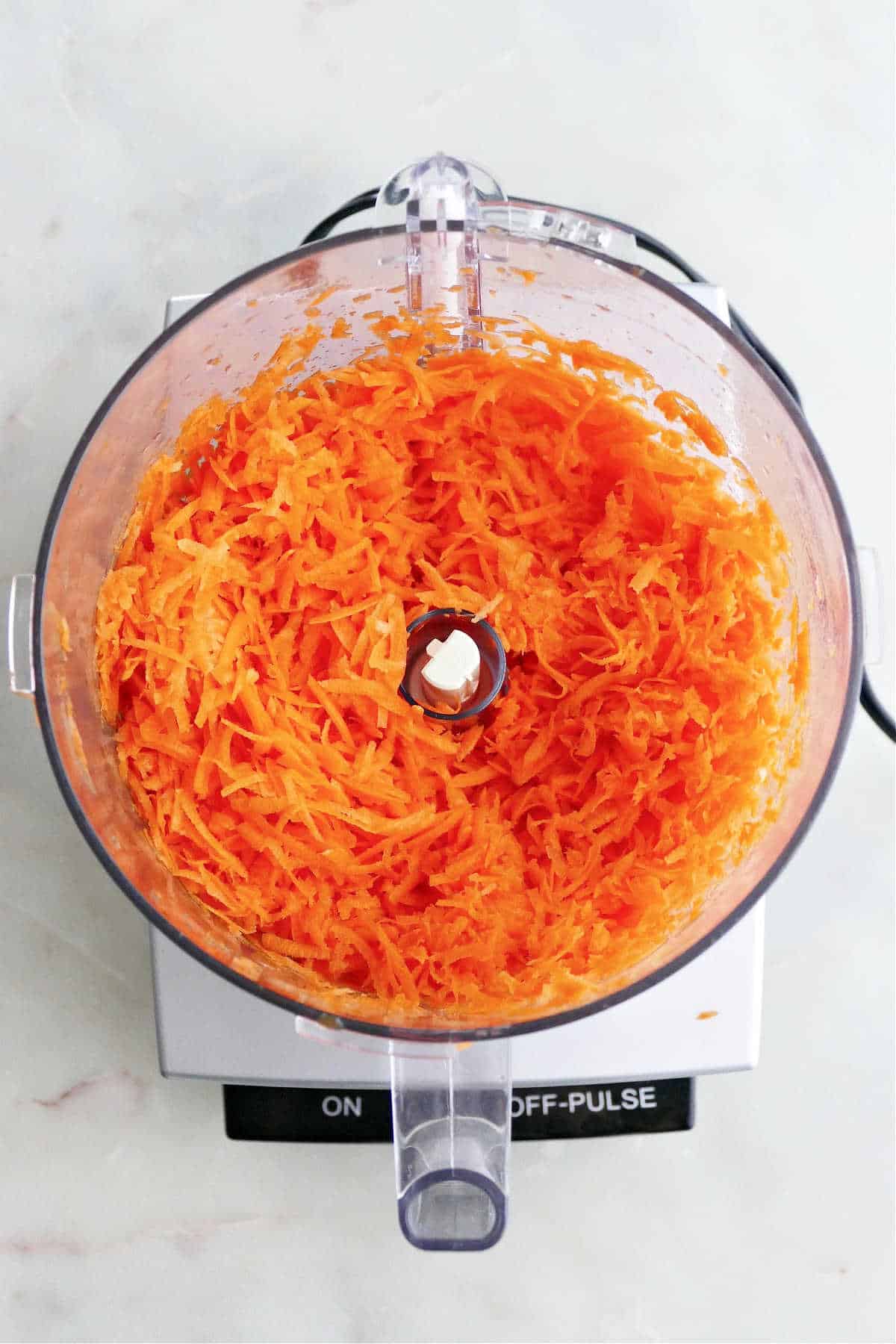 grated carrots in a food processor without lid on top of a counter