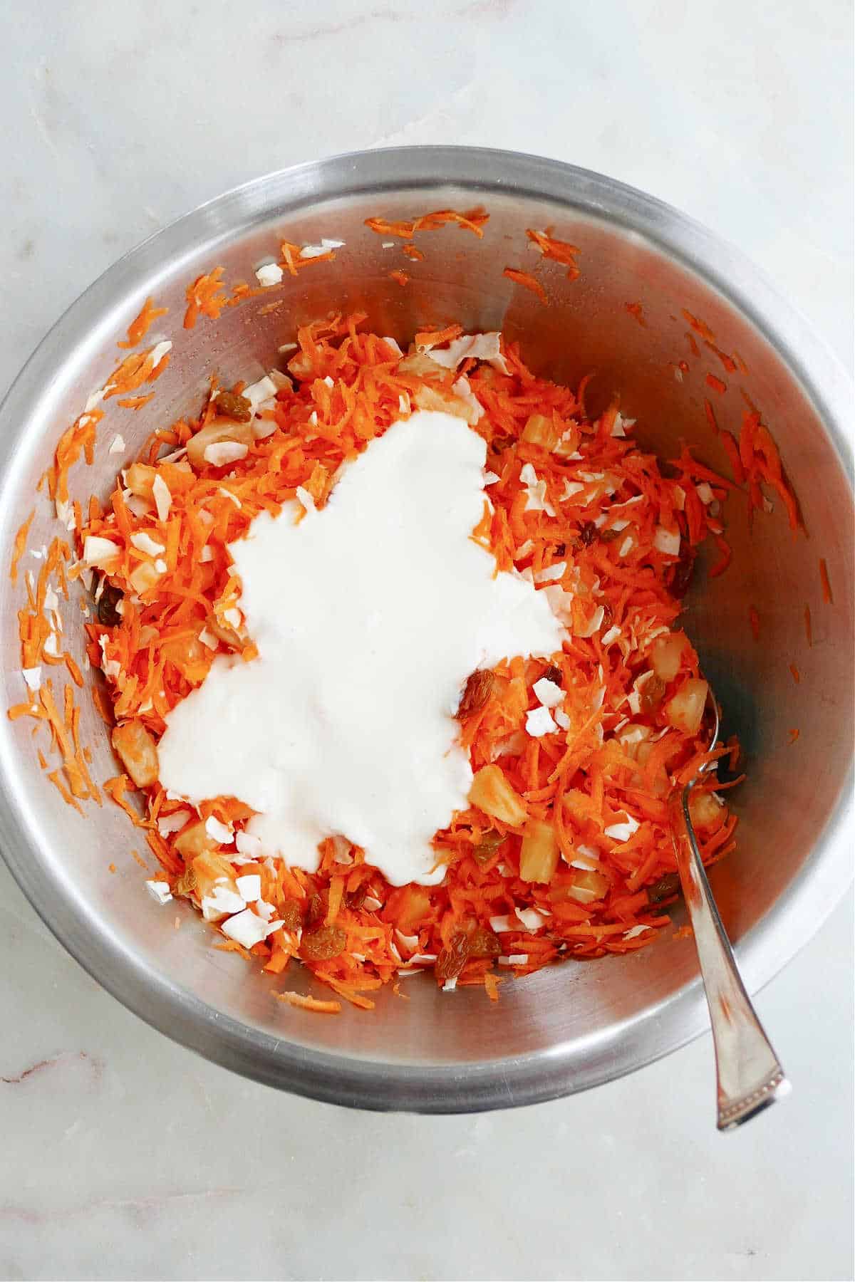 carrot raisin salad ingredients mixed together with yogurt dressing poured on top in a bowl