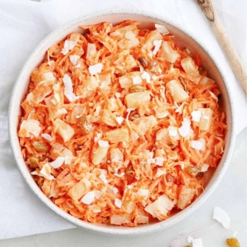 carrot raisin salad with pineapple and coconut in a serving bowl on a napkin