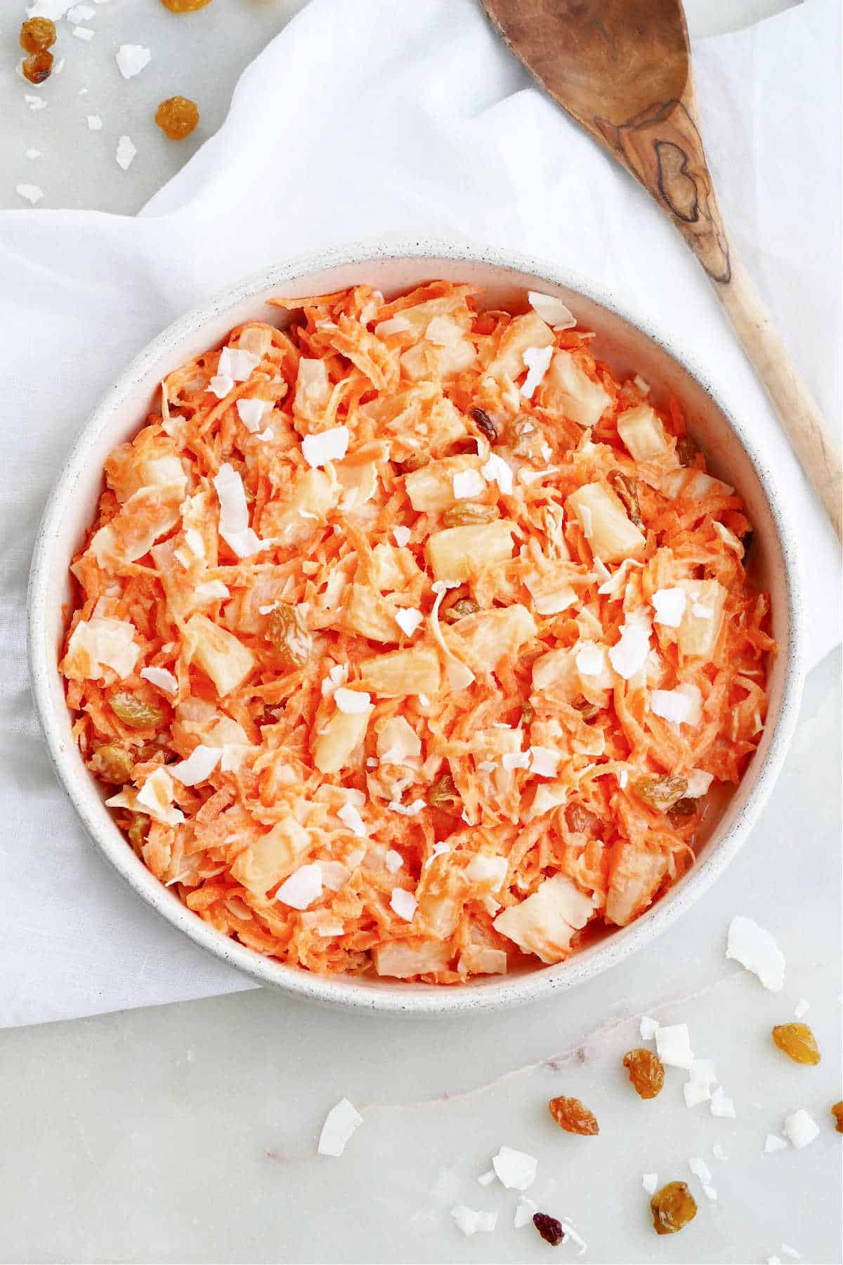 carrot raisin salad with pineapple and coconut in a serving bowl on a napkin