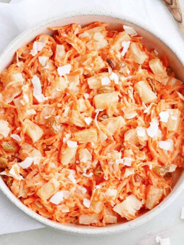 carrot raisin salad with pineapple and coconut in a serving bowl on a napkin
