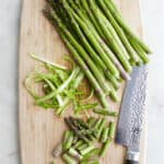 trimmed aspagarus, shaved asparagus, and sliced asparagus next to a chef's knife on a cutting board