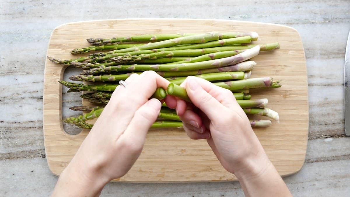 woman snapping off the end of an asparagus spear over a cutting board