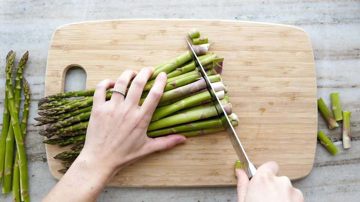 woman trimming asparagus spears with a knife on a cutting board