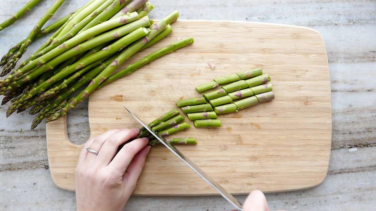 woman slicing asparagus into 1-inch spears with a knife on a cutting board