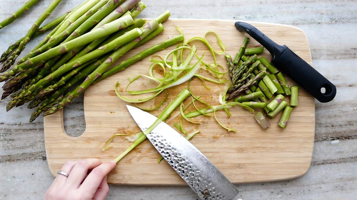 woman shaving asparagus with a chef's knife over a cutting board
