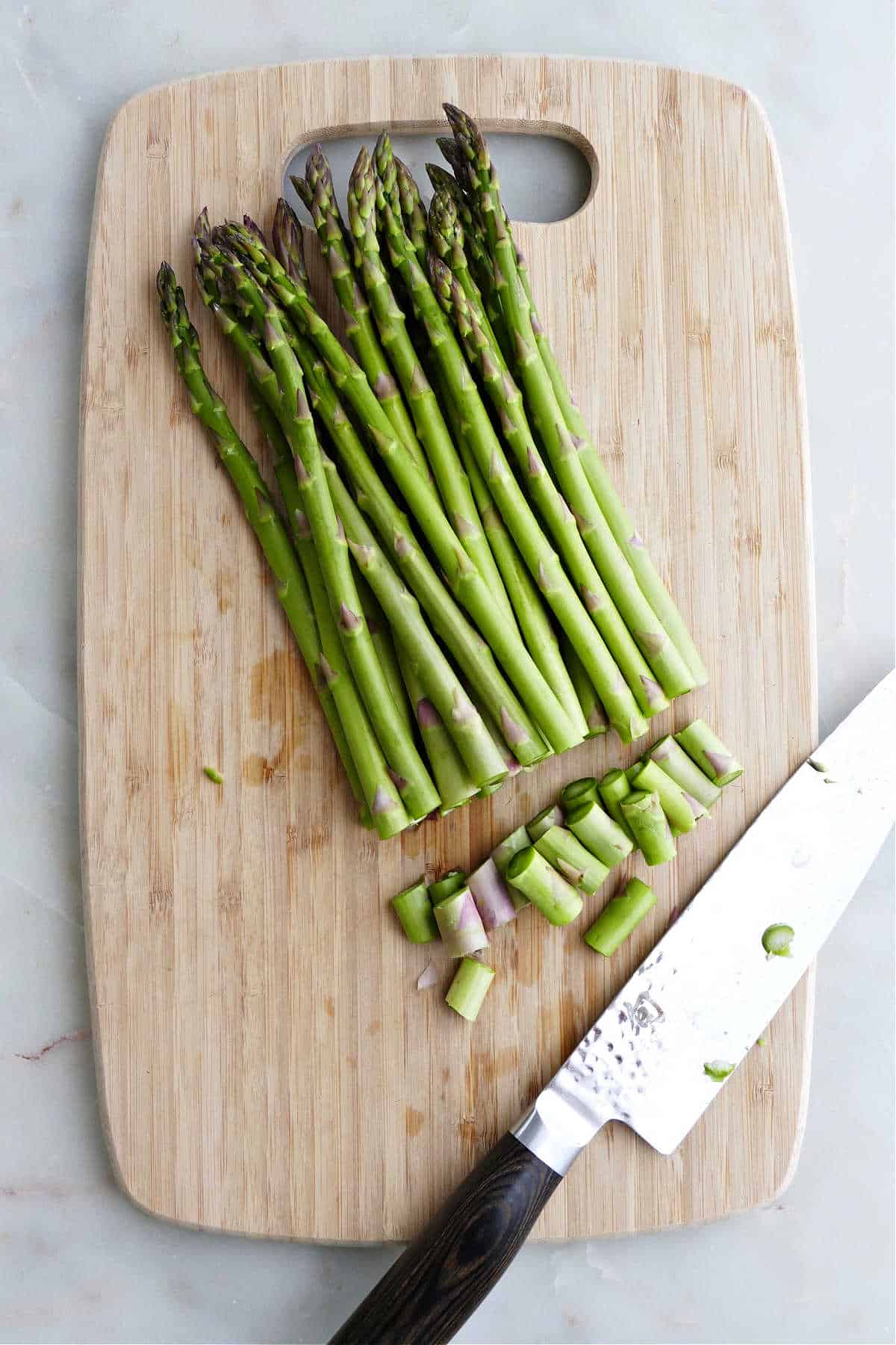 asparagus spears with bottoms trimmed off on a cutting board next to knife