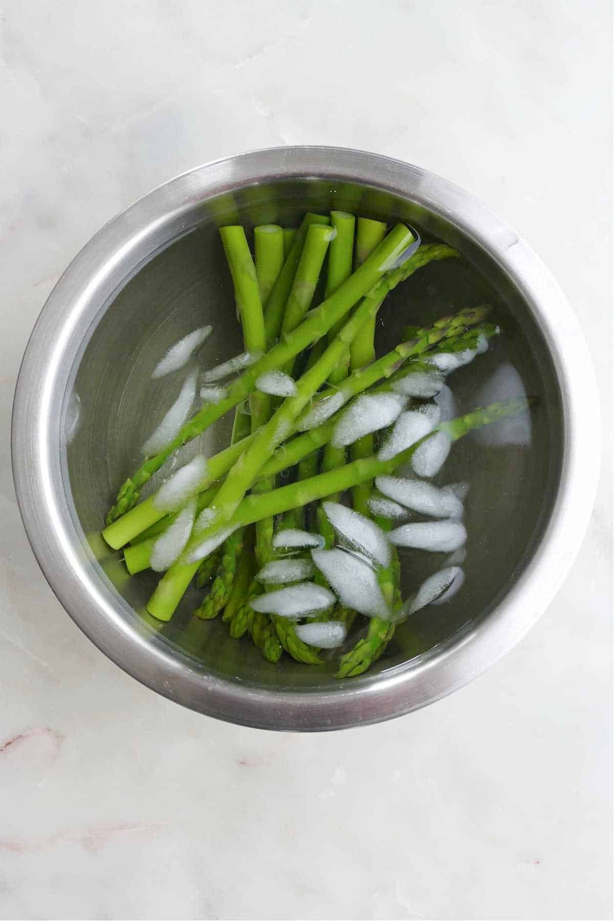 asparagus spears submerged in a bowl of ice water on a counter