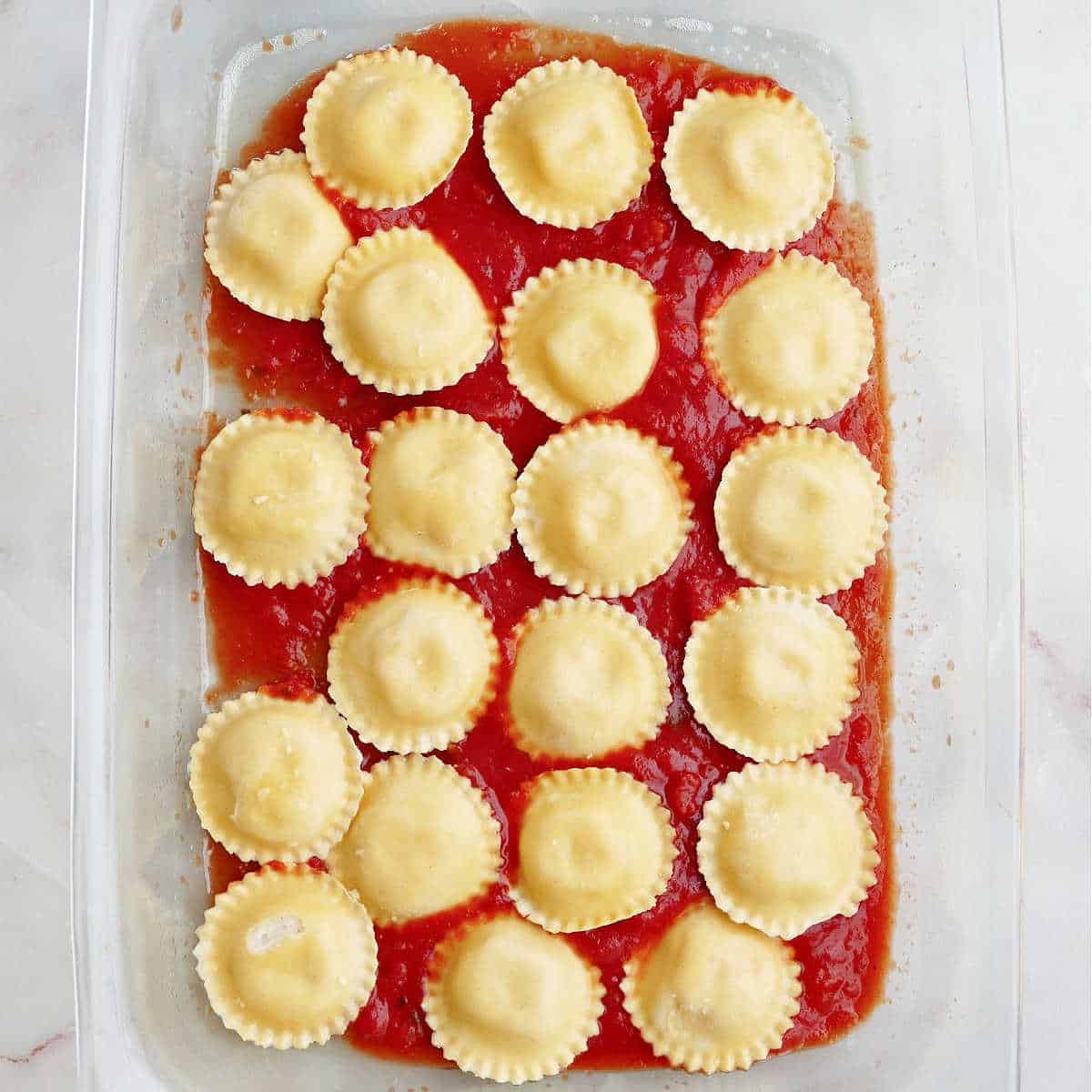 ravioli on top of marinara sauce in a glass baking dish on a counter