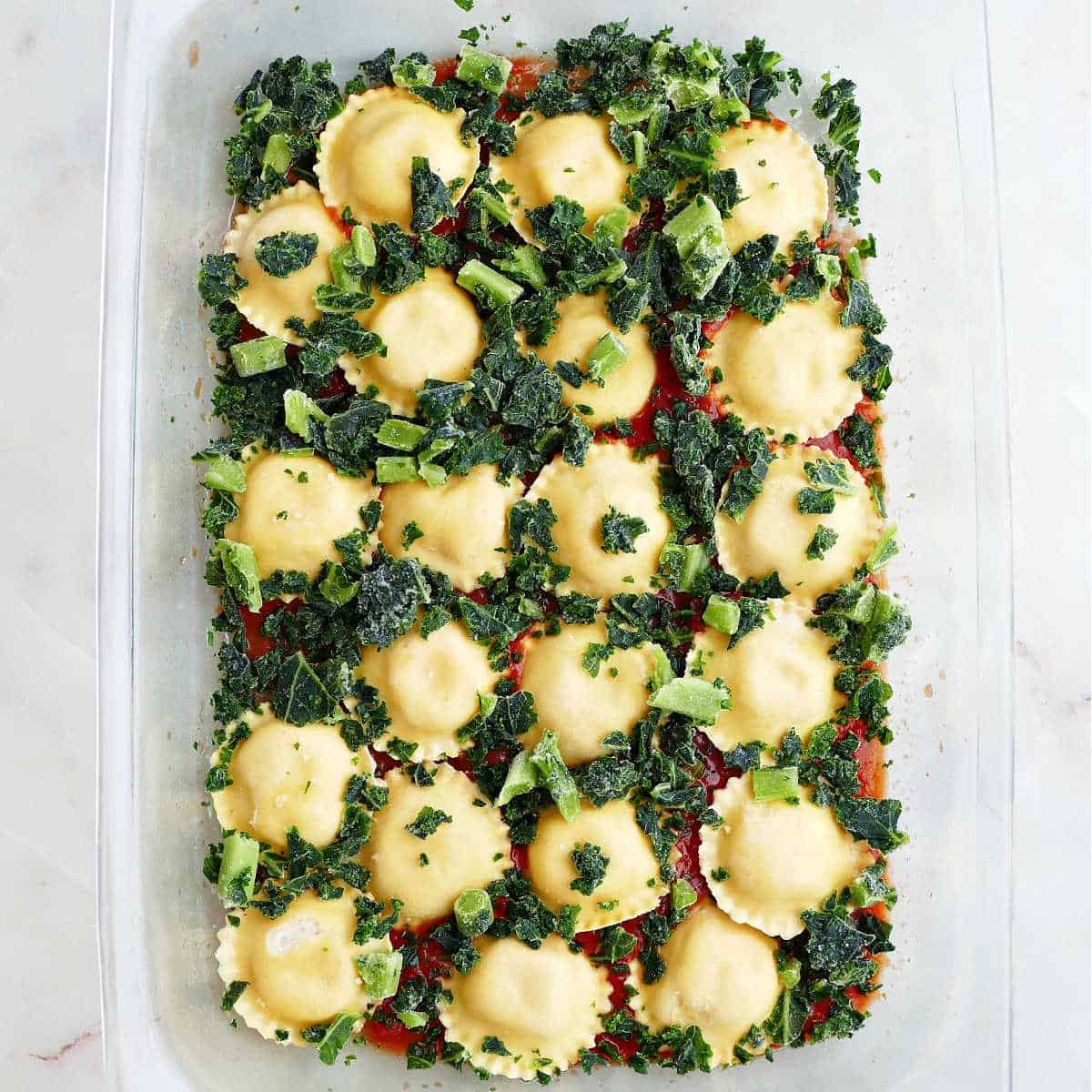 ravioli, marinara sauce, and chopped frozen kale spread out in a baking dish