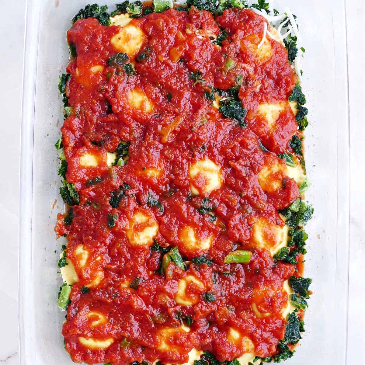 layers of ravioli, marinara sauce, and chopped frozen kale in a glass baking dish