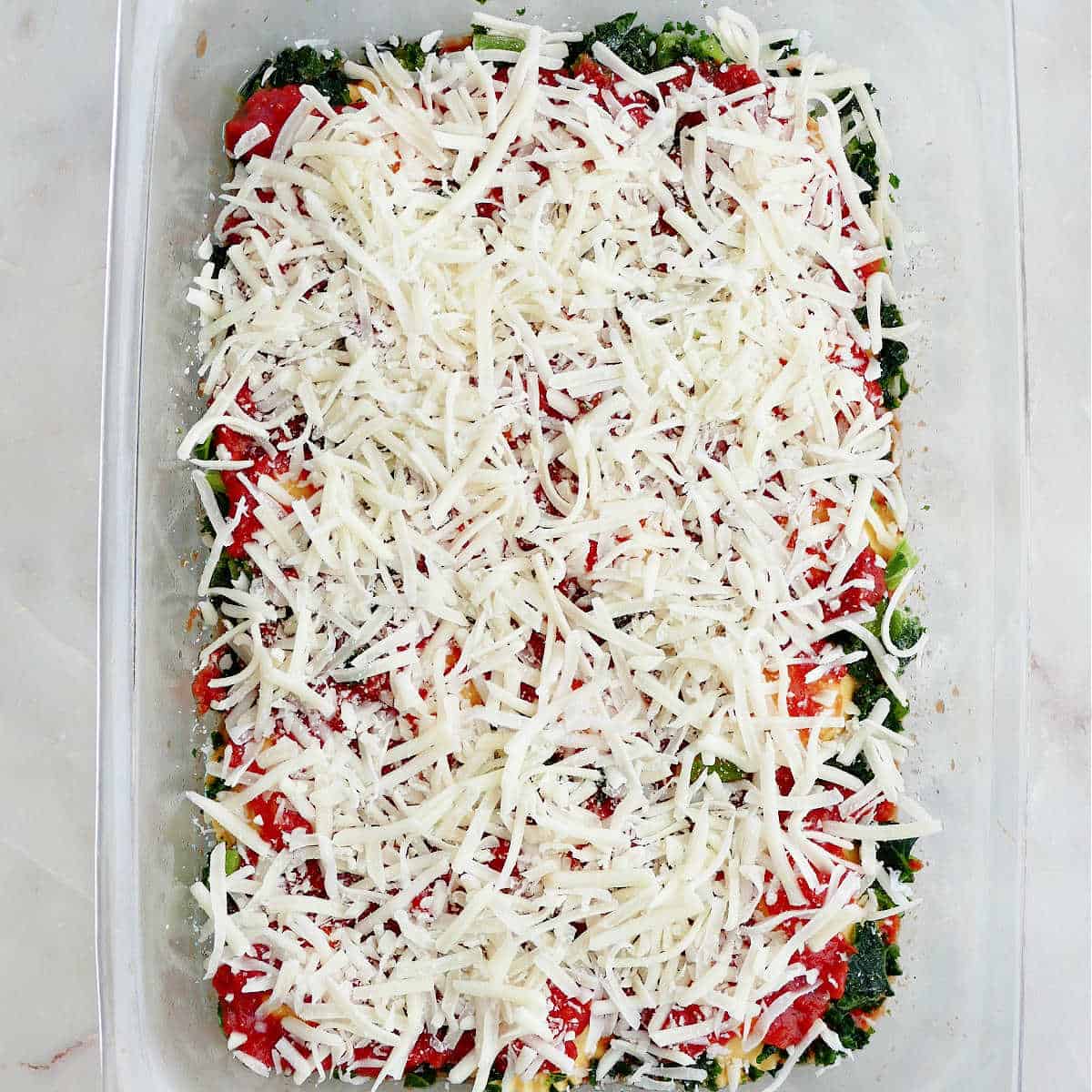 layers of ravioli, frozen kale, marinara sauce, and shredded cheese in a baking dish