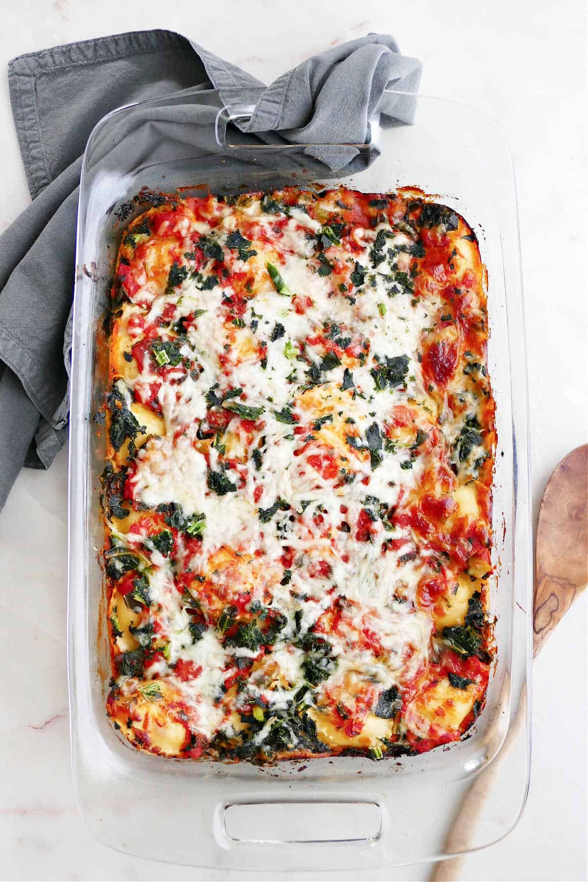 baked ravioli casserole with kale in a glass dish on a counter
