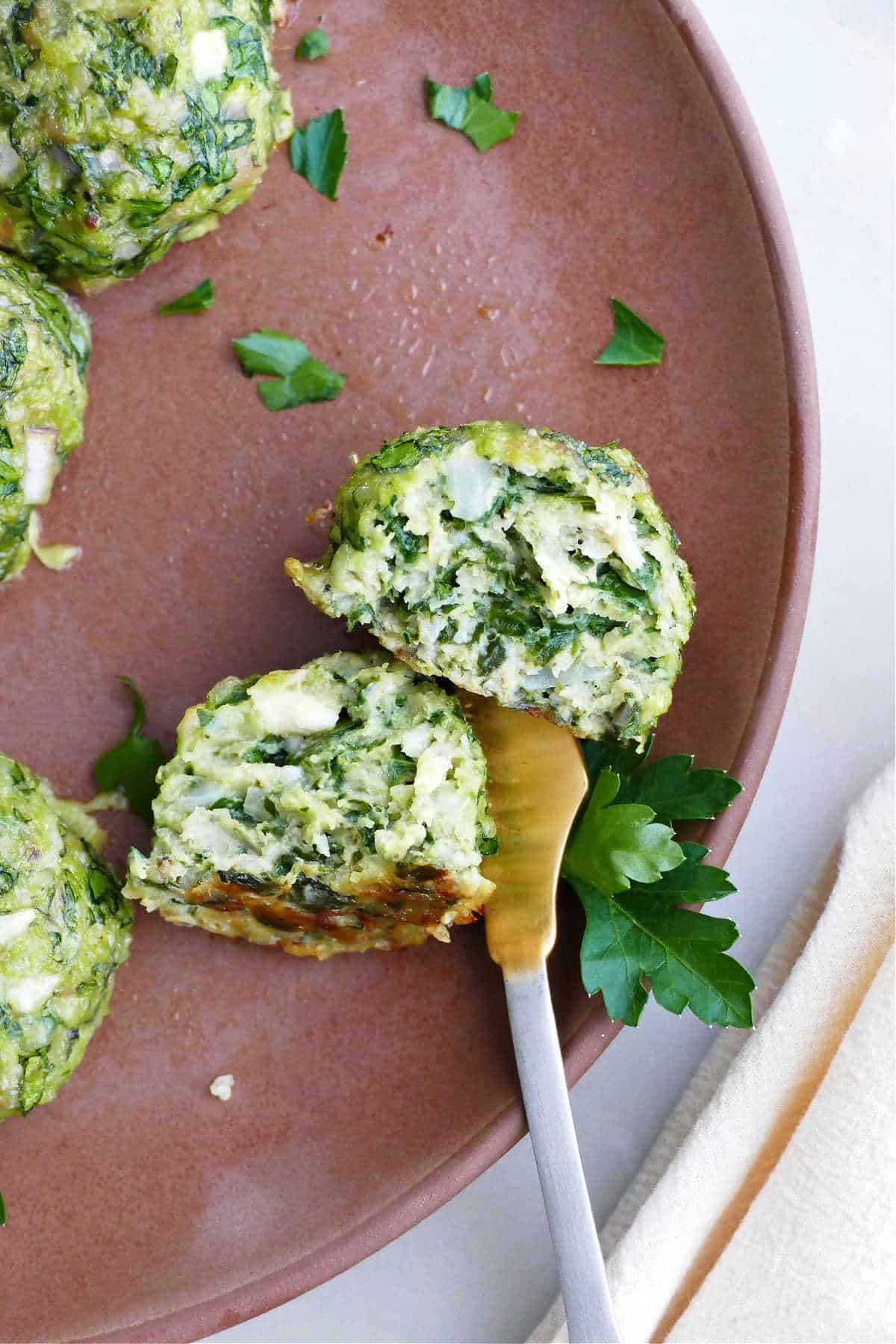spinach chicken meatball sliced in half with a fork in it on a plate