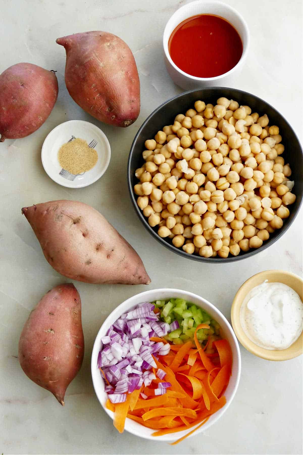 sweet potatoes, chickpeas, buffalo sauce, chopped vegetables, ranch, and garlic powder on a counter