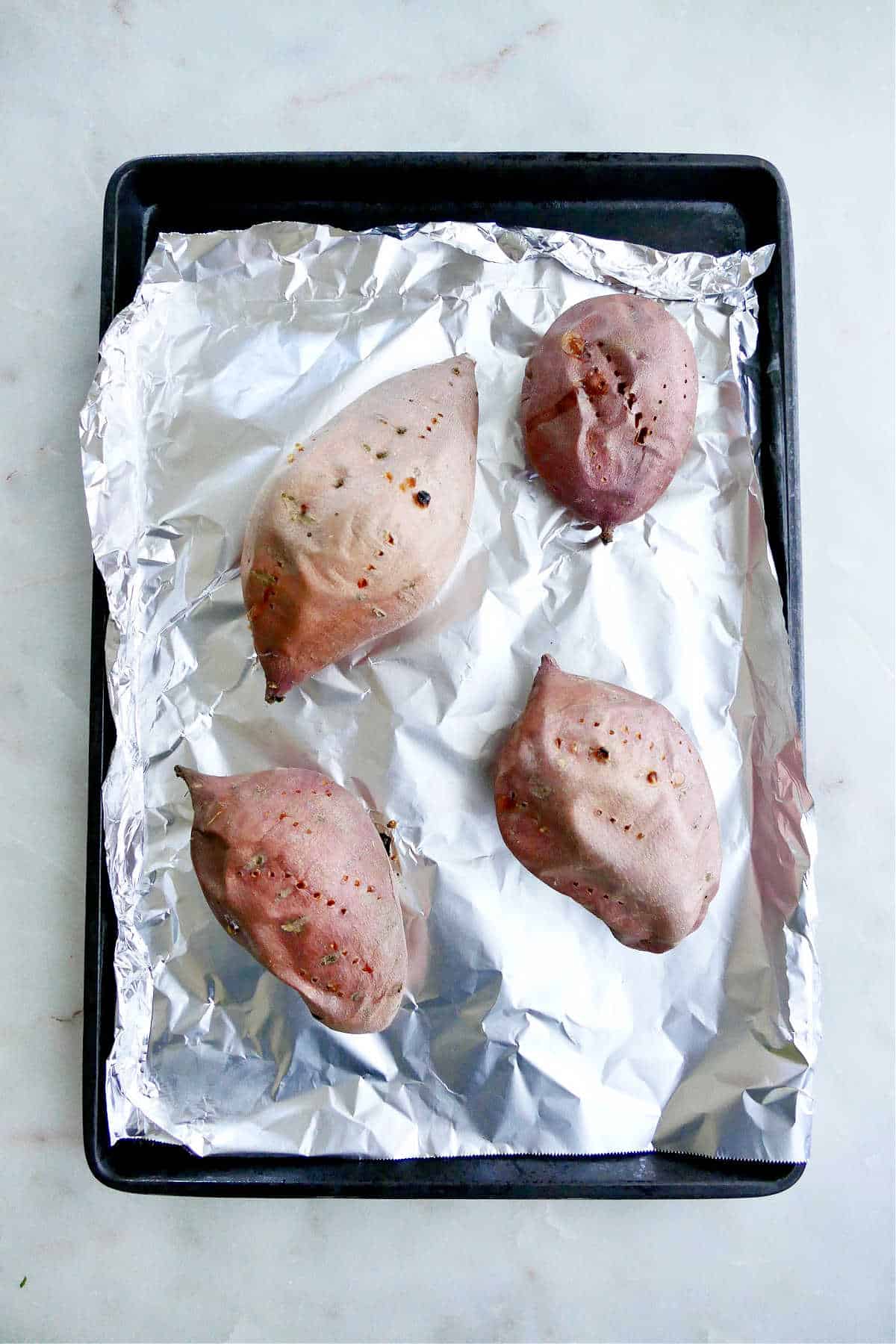 four roasted sweet potatoes on a baking sheet lined with foil