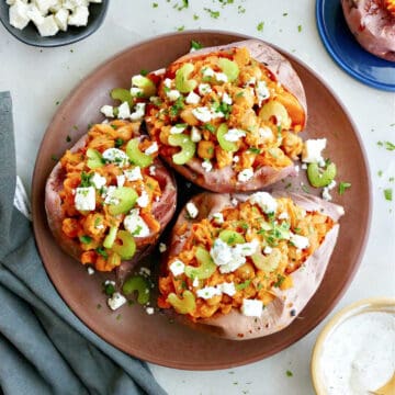 three sweet potatoes stuffed with buffalo chickpeas on a serving plate on a counter