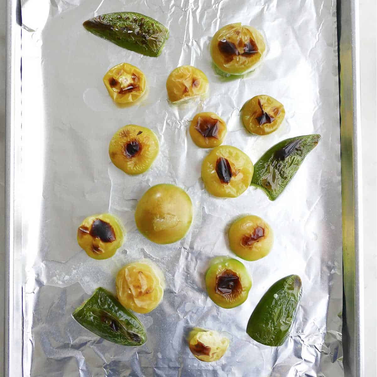 roasted tomatoes and jalapenos on a baking sheet lined with foil