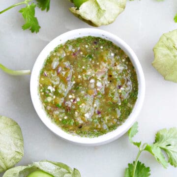 salsa verde in a small serving bowl surrounded by tomatillos and cilantro