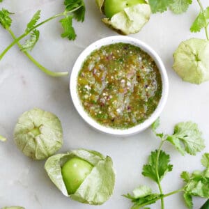 Salsa verde in a small serving bowl surrounded by tomatillos and cilantro.
