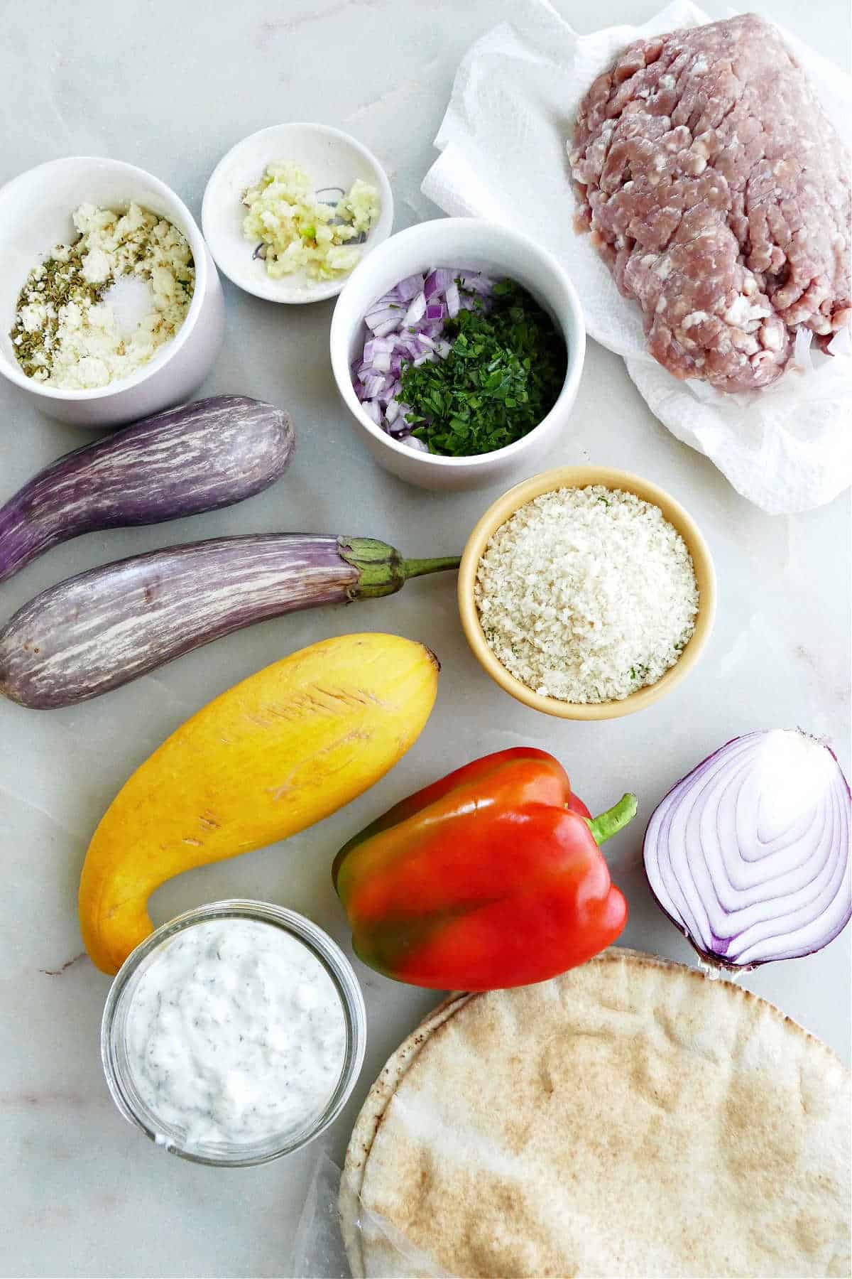 ground turkey, breadcrumbs, garlic, seasonings, onion, vegetables, pita, and yogurt on a counter