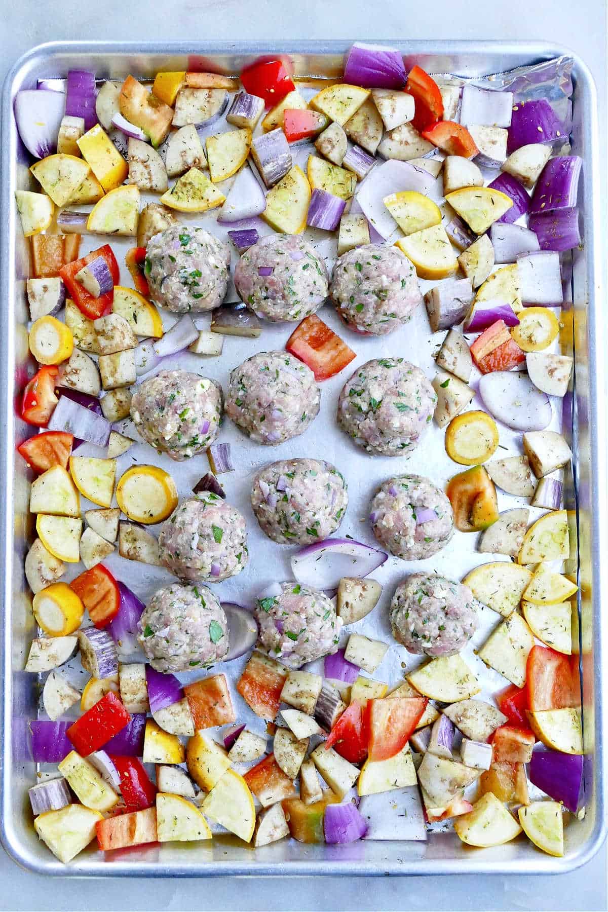 Turkey meatballs and chopped vegetables spread out on a baking sheet lined with foil