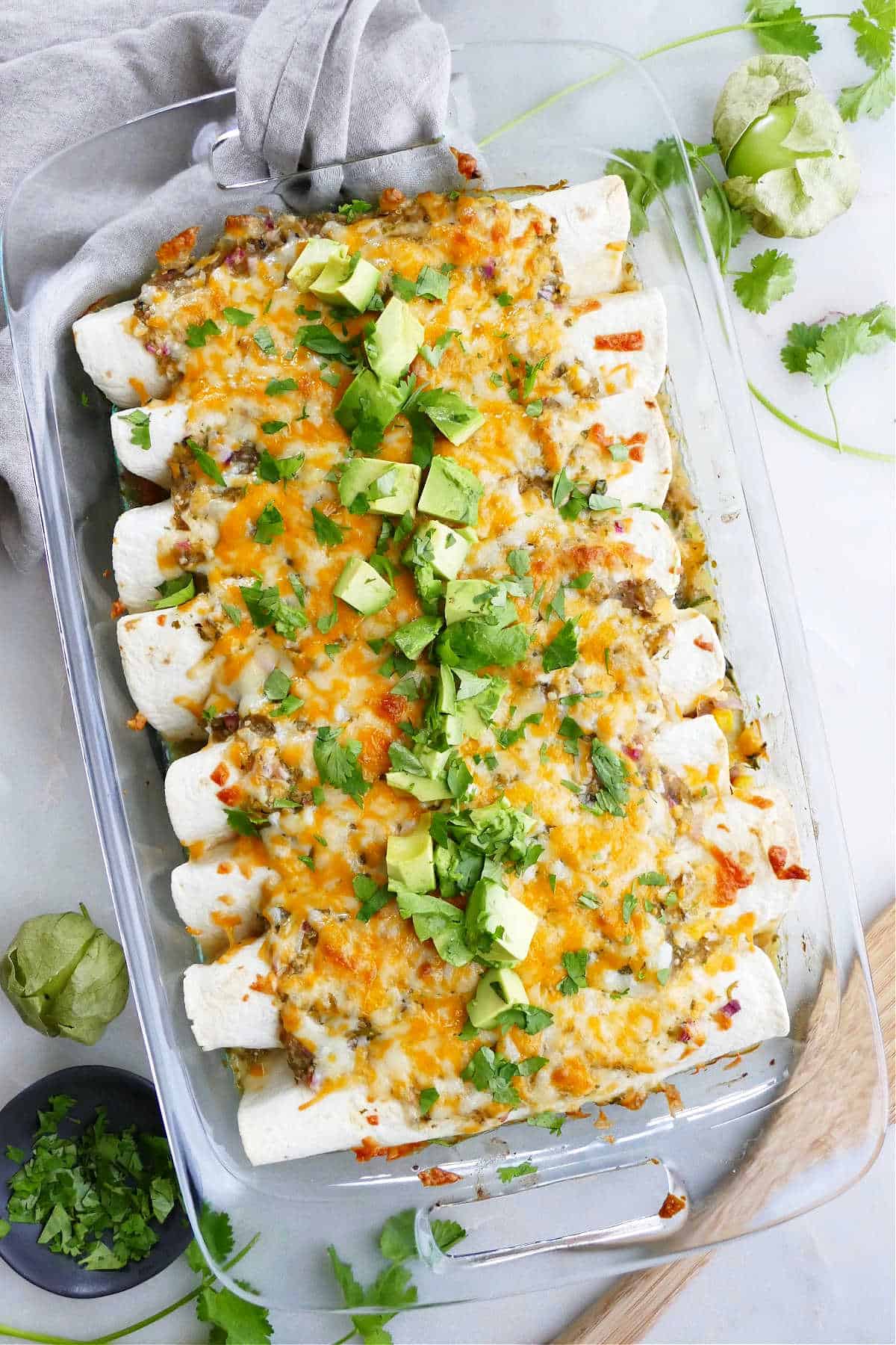 vegetarian enchiladas verdes in a baking dish topped with avocado and cilantro