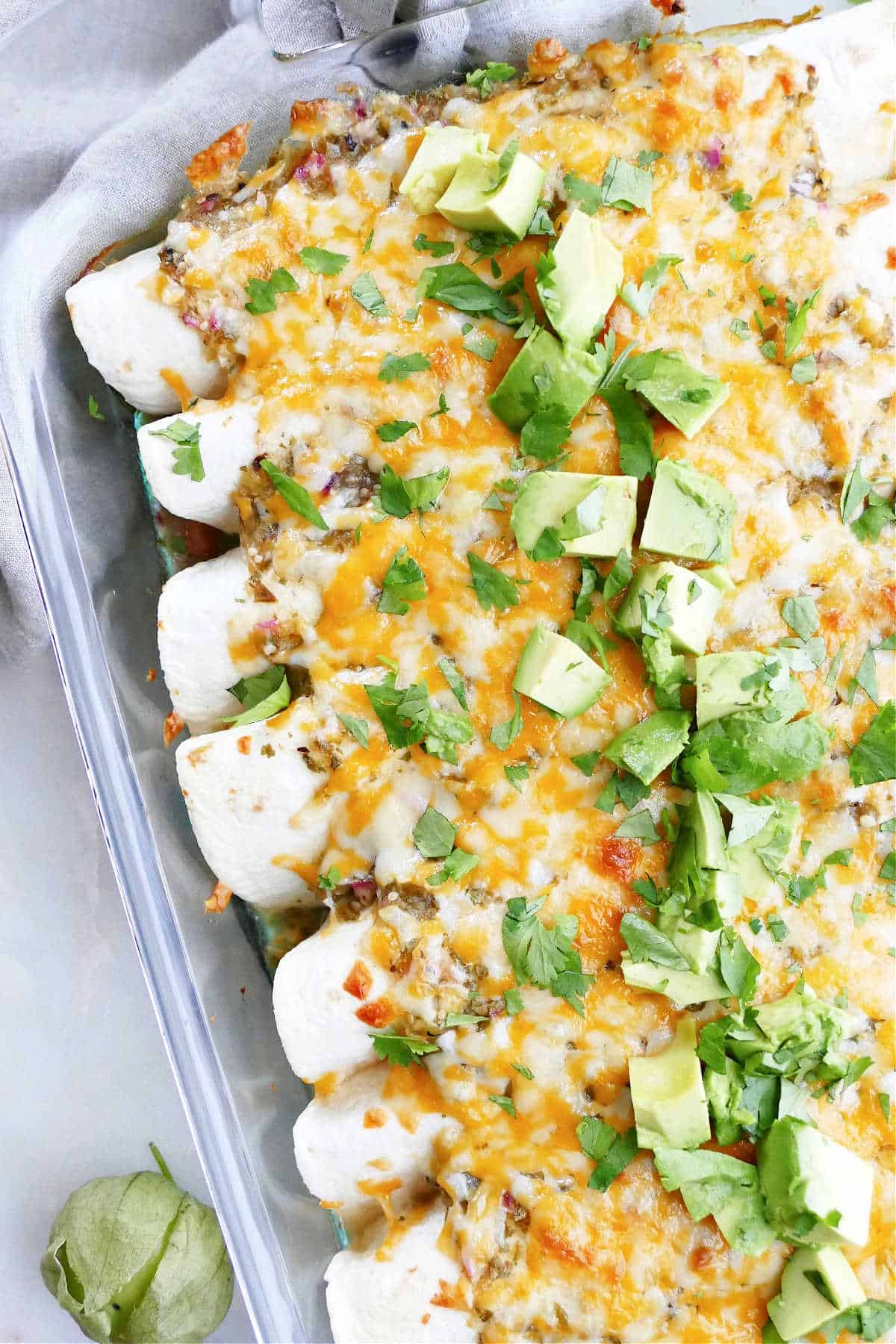 vegetarian enchiladas verdes in a dish topped with avocado and cilantro
