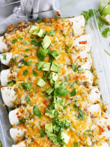 vegetarian enchiladas verdes in a dish topped with avocado and cilantro