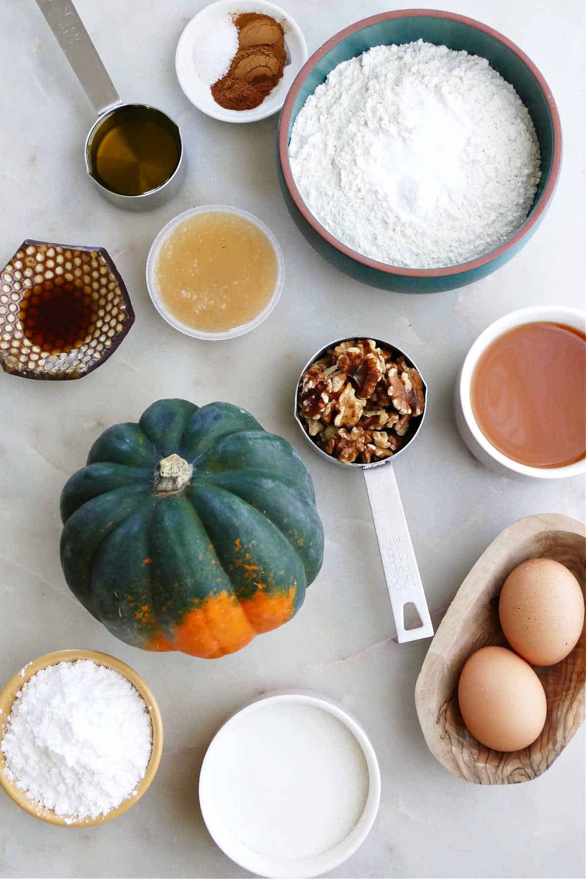 flour, seasonings, olive oil, applesauce, vanilla, walnuts, eggs, acorn squash, and sugars on a counter