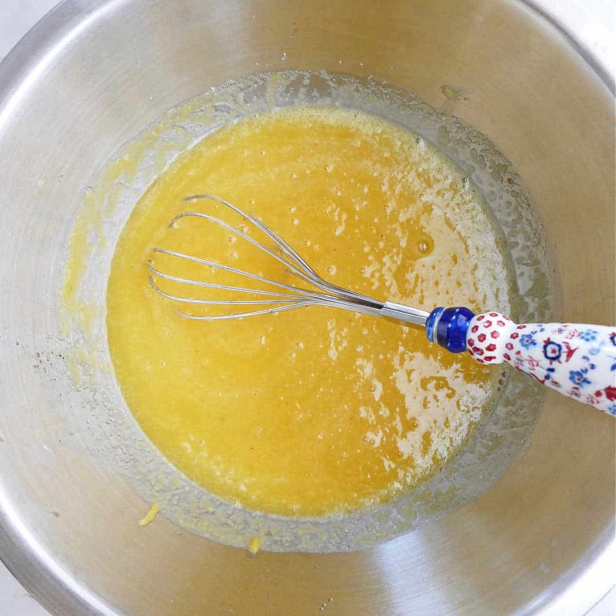 mixing bowl with olive oil, applesauce, eggs, and sugar on a counter